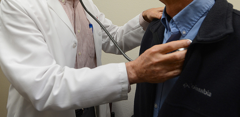 A doctor holds a stethoscope up to a person's heart.