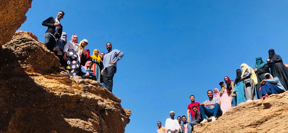 Roughly 20 people from Project ECHO in Sudan take a group photo standing on a rock formation.