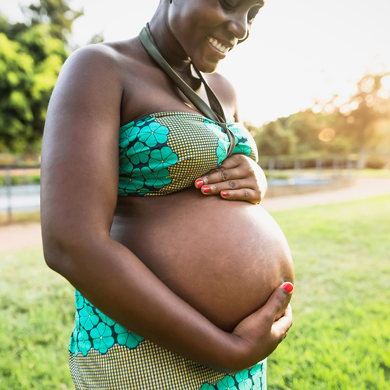 A pregnant woman looks down and smiles as she holds her bare stomach.