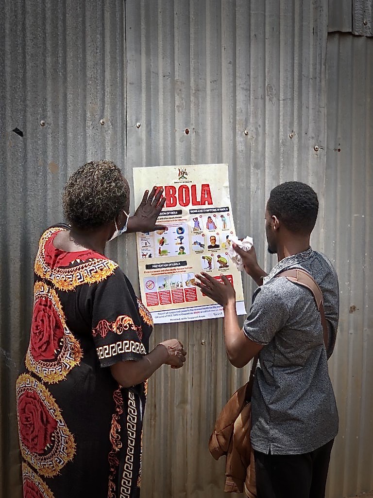 Two community health workers in Kampala hang a poster designed to combat misinformation on the Sudanese strain of the Ebola virus. 