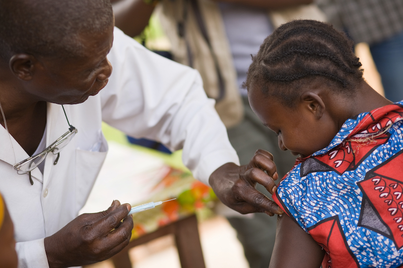 A male doctor in Africa gives a vaccine to a child.
