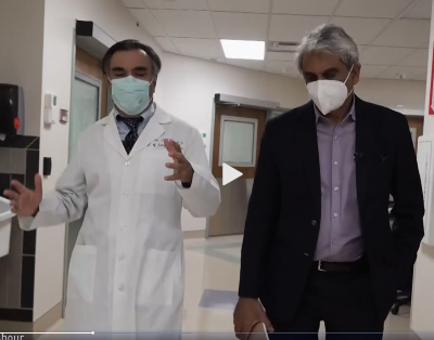 Dr Arora, left, talks with PBS NewsHour Fred de Sam Lazaro in a hospital setting, both wear face masks