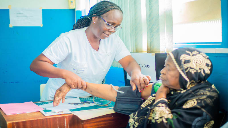 A female African health provider put a blood pressure cuff on a patient 