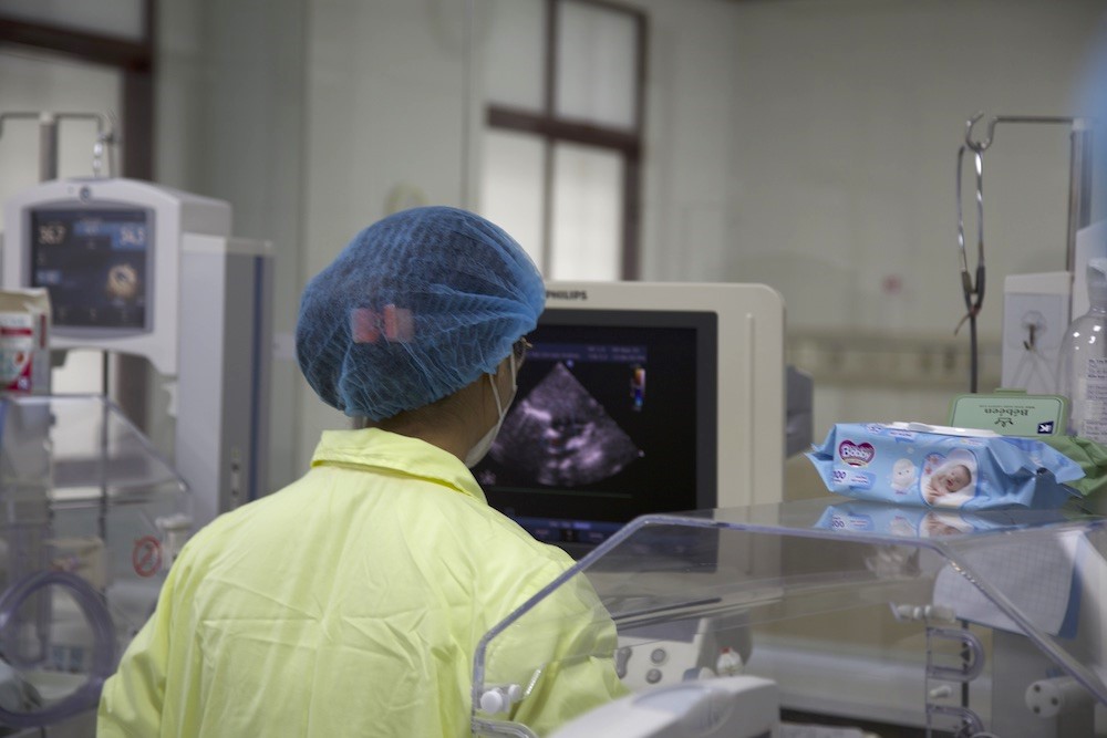 A tech, wearing protective head net, looks at the image of an ultrasound