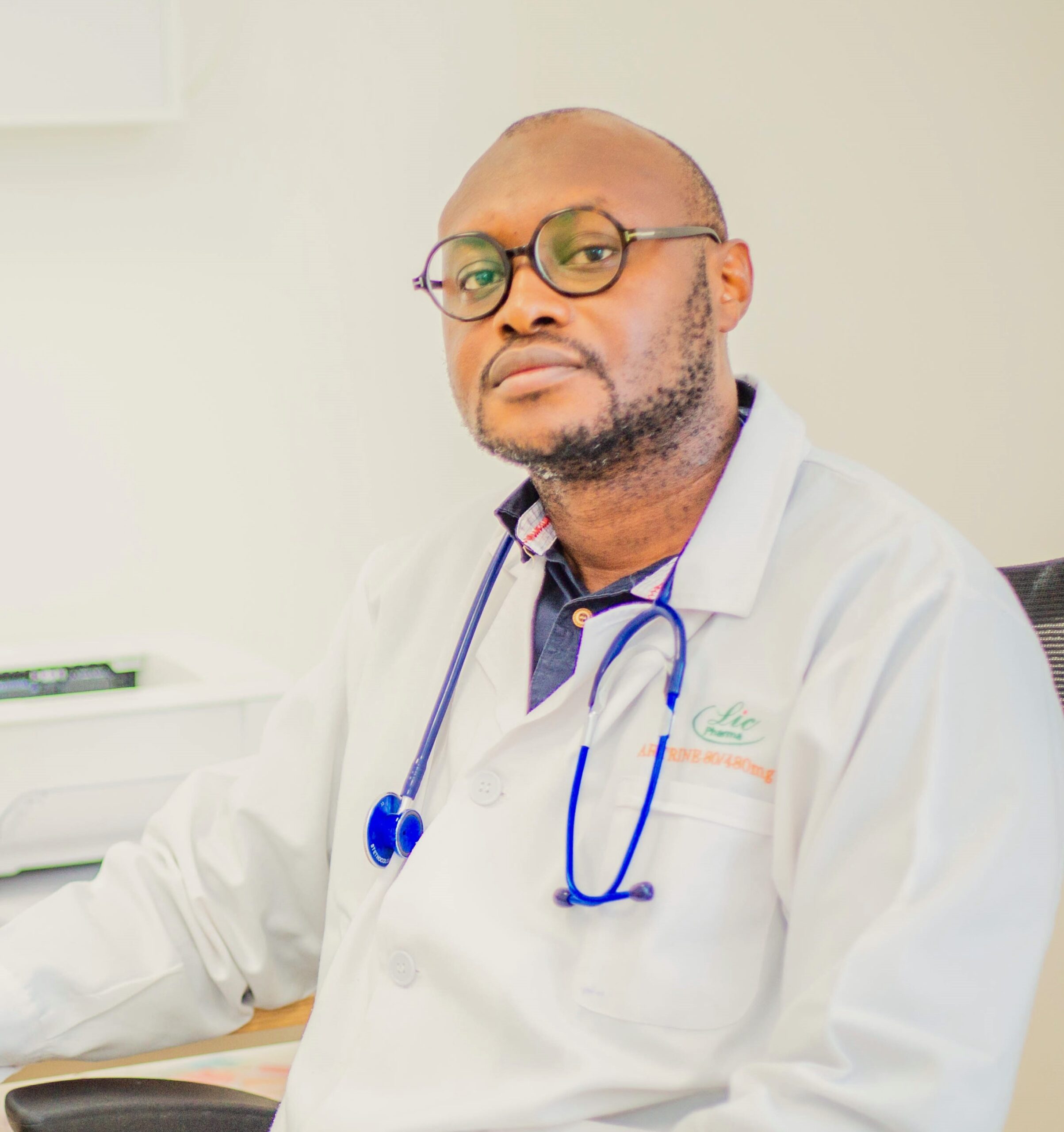 An African doctor sits at a desk, wearing a white lab coat and blue stethoscope