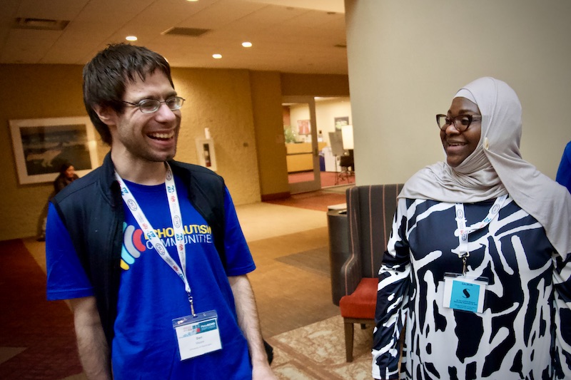A light skin-tone man with glasses laughs with a dark skin-tone woman in a hijab at the 2023 MetaECHO conference