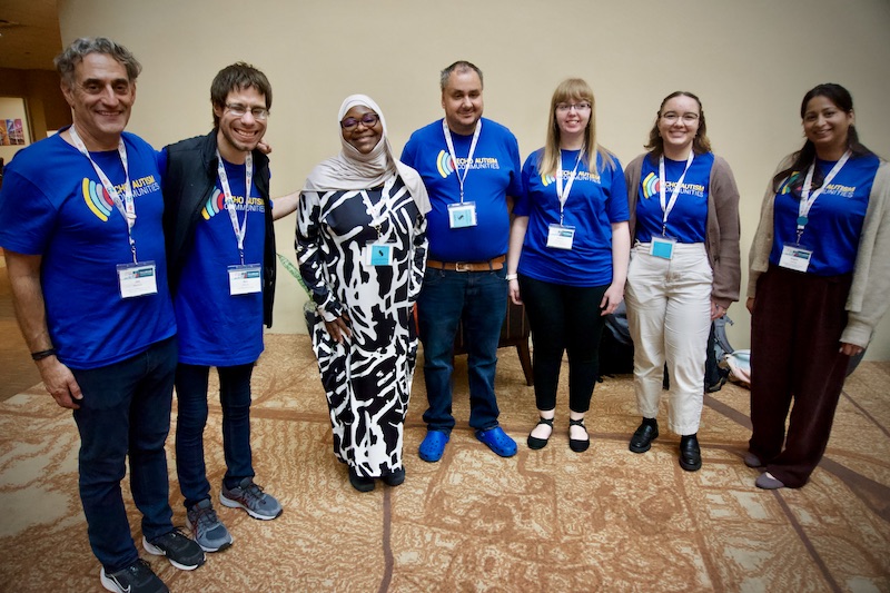 Seven people in the ECHO Autism community, including 3 men and 4 women with varying heights and skin tones, and one woman in a hijab, stand together.