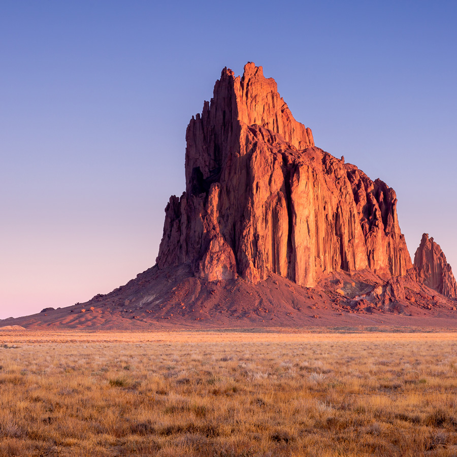 Tall cliff rising out of New Mexico dessert at sunrise.