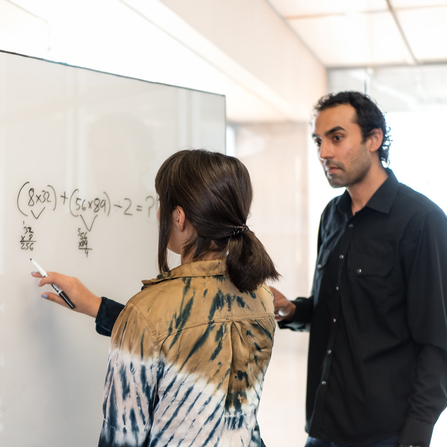 Two people standing next to a white board.