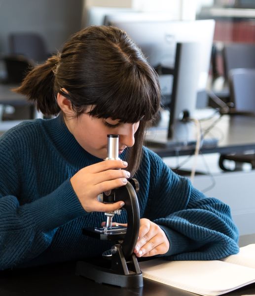A middle school aged girl looks into a microscope