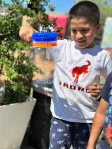 An elementary aged boy smiles as he holds a bubble wand