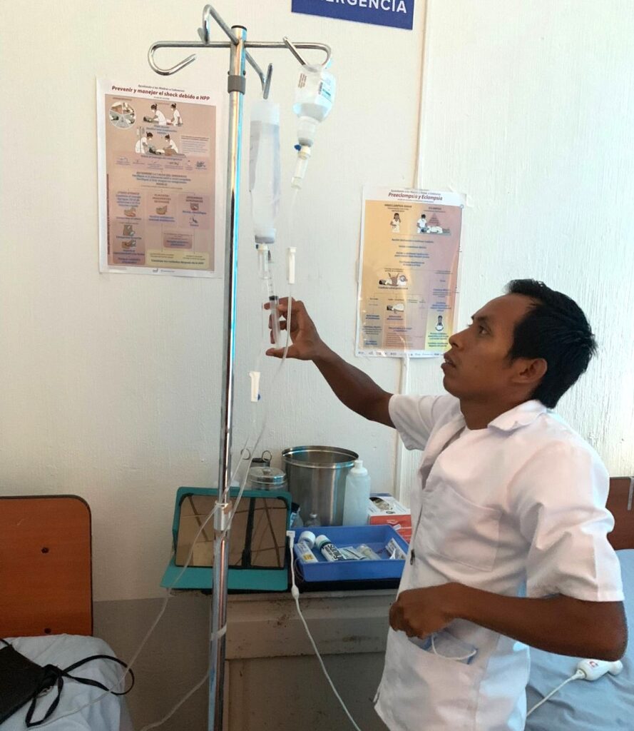 A male nurse injects a medication into a saline drip in a clinic. San Ramon, Guatemala