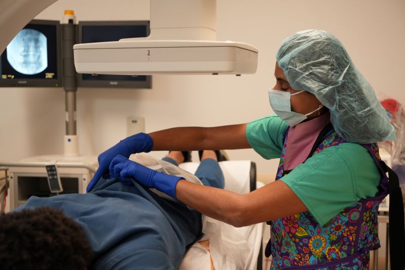 Dr. Radhika Grandhe wears PPE and adjusts a patient's clothing who is lying under a scanner