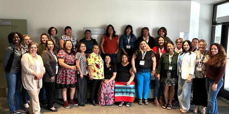 A photo of about 24 people, mostly female, standing in front of a wall