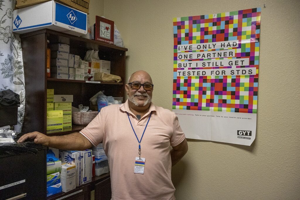 Joe Rivas standing in front of a case of harm reduction and STI testing supplies for his clients