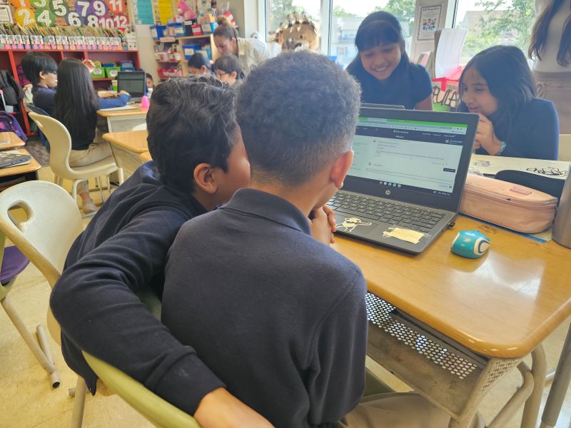 Two children sit closely together looking at a laptop