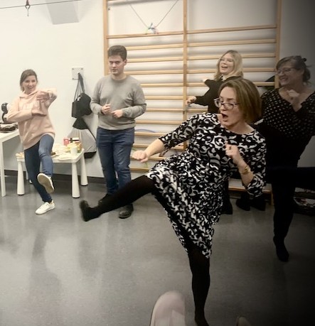 A woman kicks to her side. Behind her stand adolescents imitating physical movements