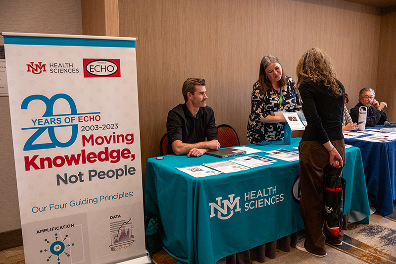 Two members of the SCAETC program team sit behind a table speaking with a conference attendee at the 2025 AETC Conference in Albuquerque, New Mexico.