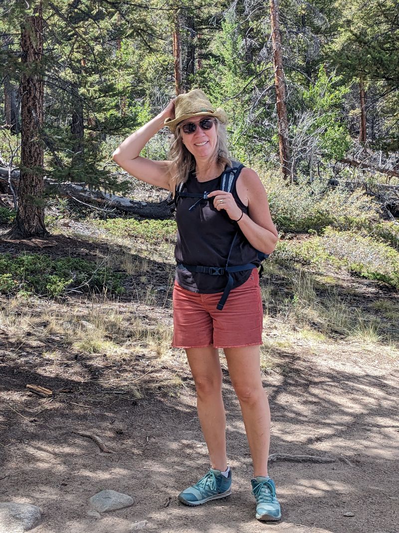 Andrea Zurawski stands in a forest. She touches her sunhat.