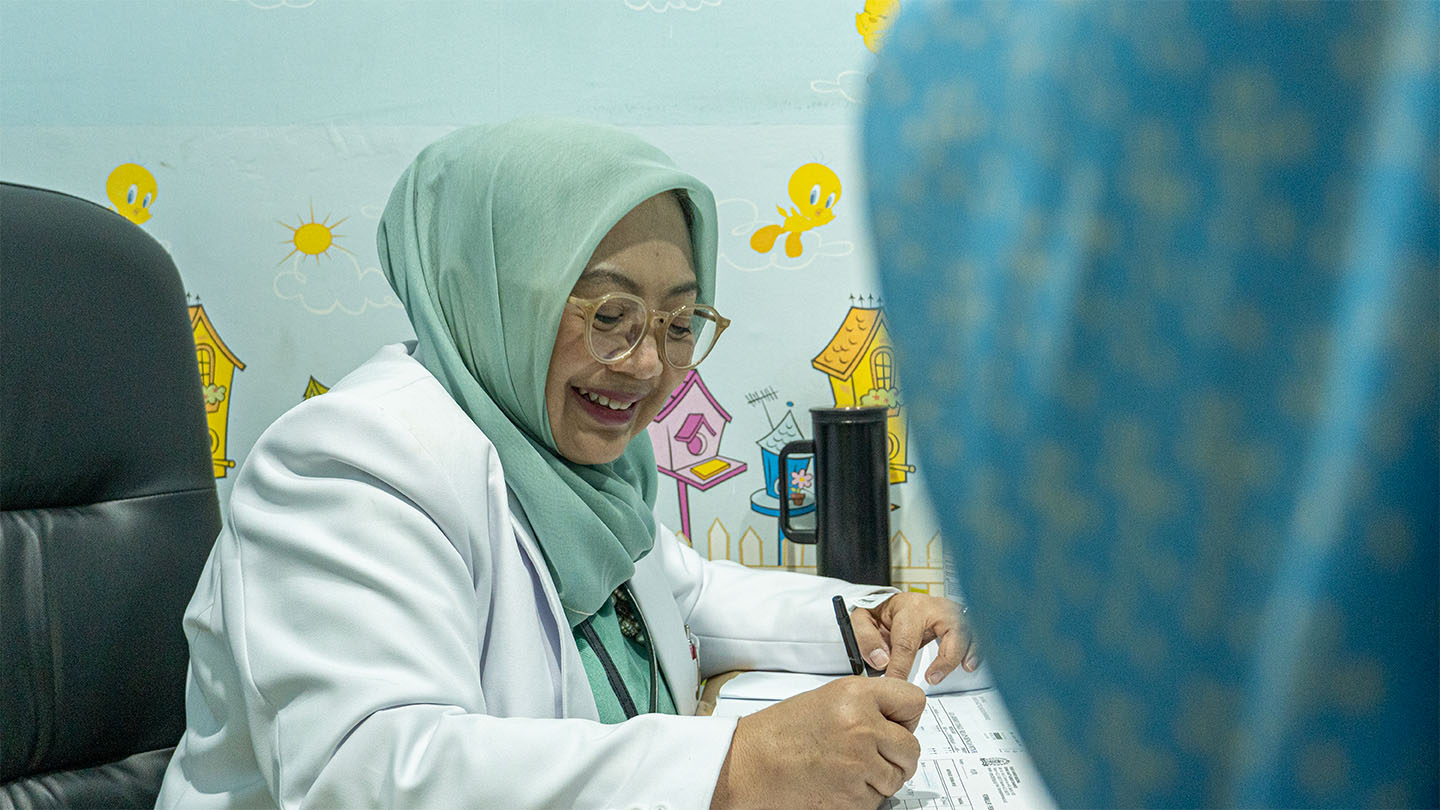 A female doctor sitting at a desk filling out some paperwork in a pediatric clinic setting.