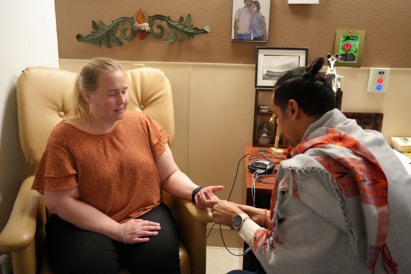 A woman holds out her hand. A man, sittin across, attaches something not visible.