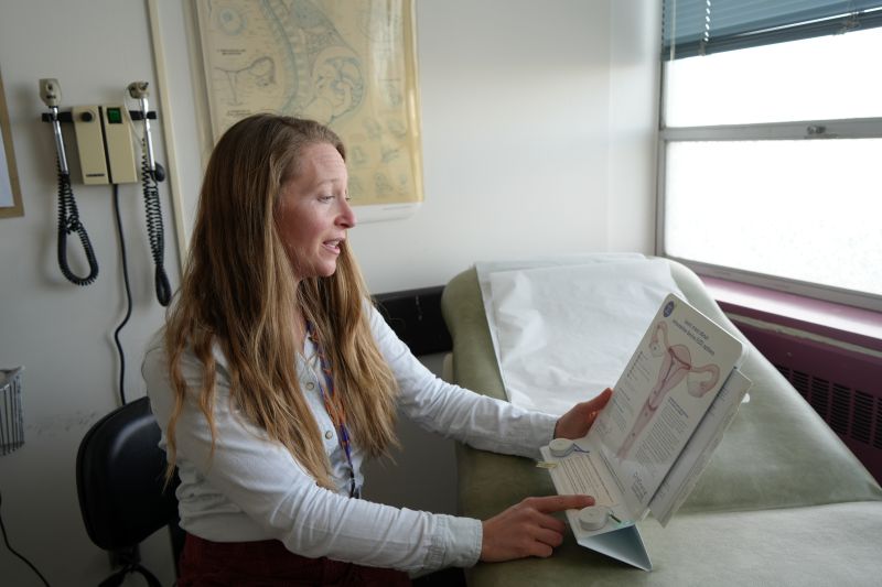 A woman in a medical office points to an illustration of a uterus.