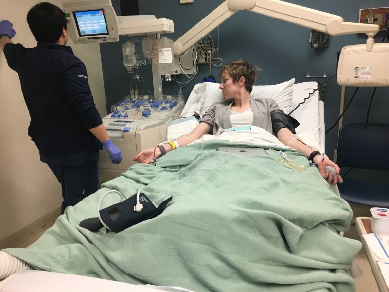 Alison Sbrana lies in a hospital bed; a health care provider stands looking at a montior.