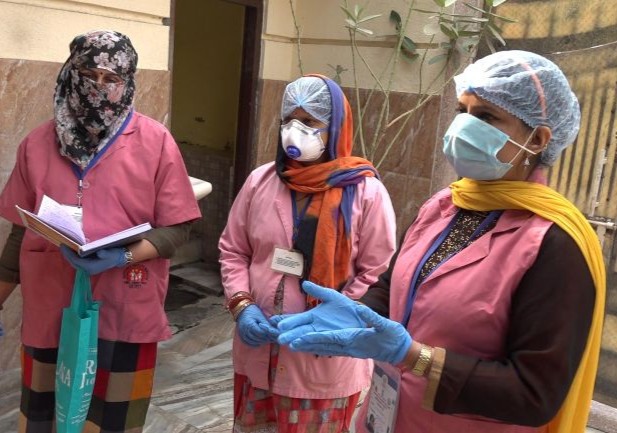 India: Three ASHAs or community health workers, wear pink vests and masks.