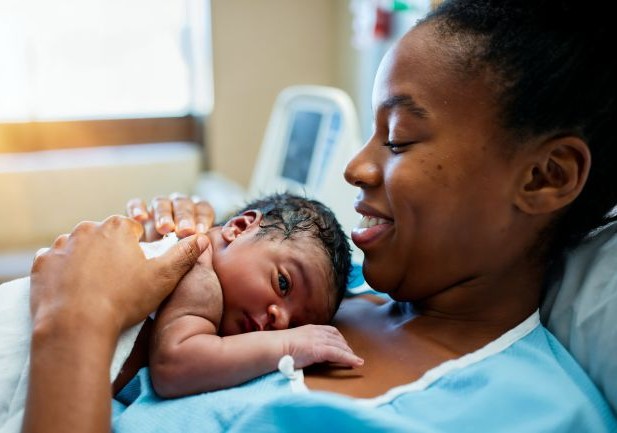 An African American mother does skin to skin with her newborn on her chest; she smiles