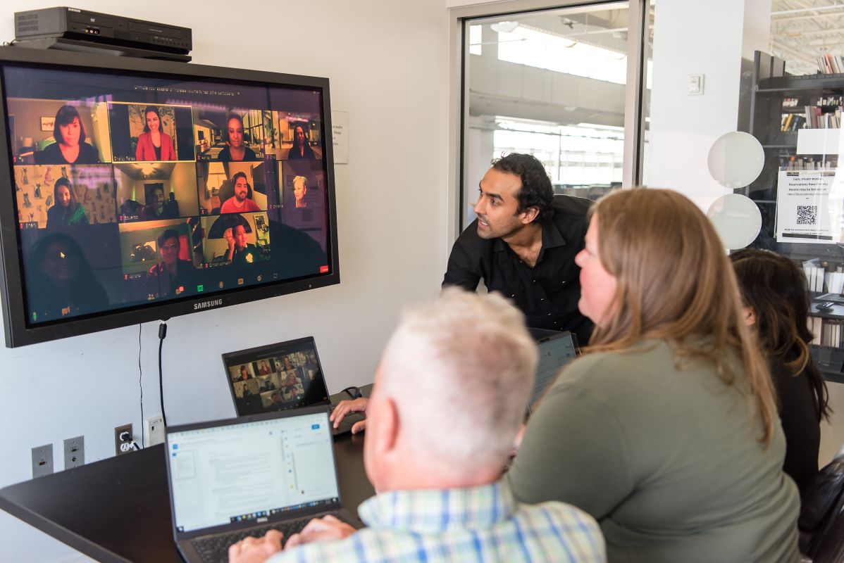 Project ECHO staff meeting in a room in front of a screen with an active Zoom ECHO session on it. 