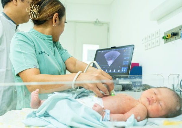 A female health care provider looks at a monitor while she does an echocardiogram on an infant, asleep