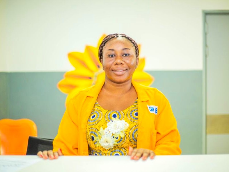A woman, wearing bright yellow, looks at the camera.