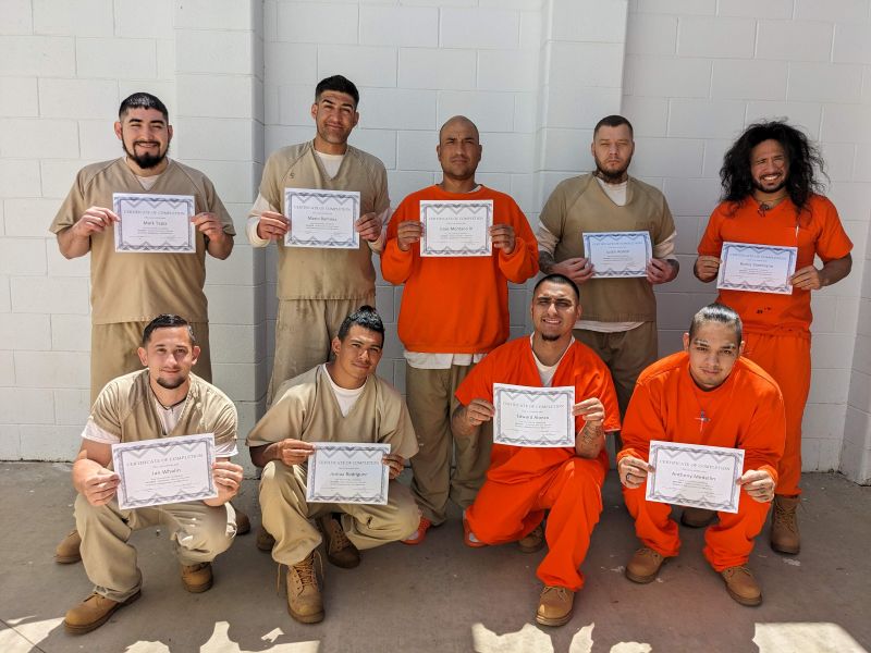 Several men pose for photo with certificates of completion from corrections facility