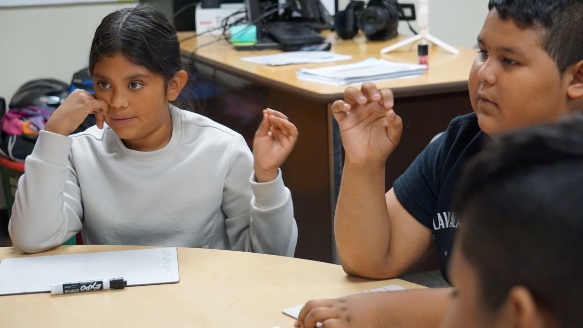 A Hispanic girl and Hispanic boy in hold up their hands during a small group lesson.