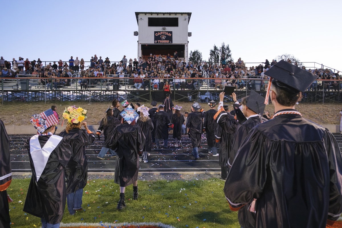 Future Ready_deGive_CaptianHS_Media Desk_June 2026 A graduation celebration on the football field of Capitan High School. Students wear graduation gowns and caps and face their parents and families, seated in the stands