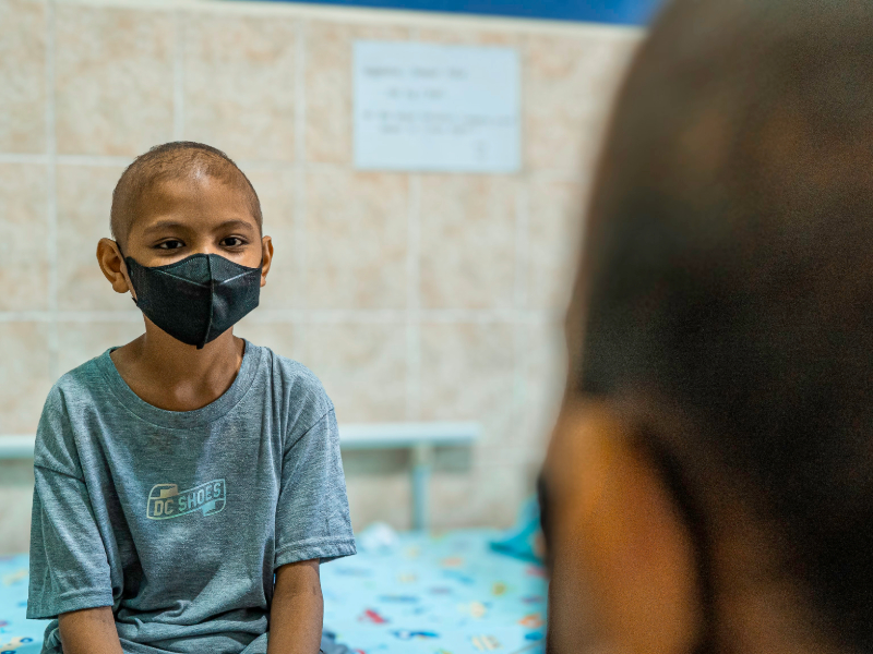 A young boy, about 6 years old, wears a mask and a hospital gown.