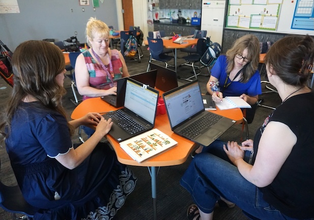 A group of teachers sit around a table with their laptops in front of them.