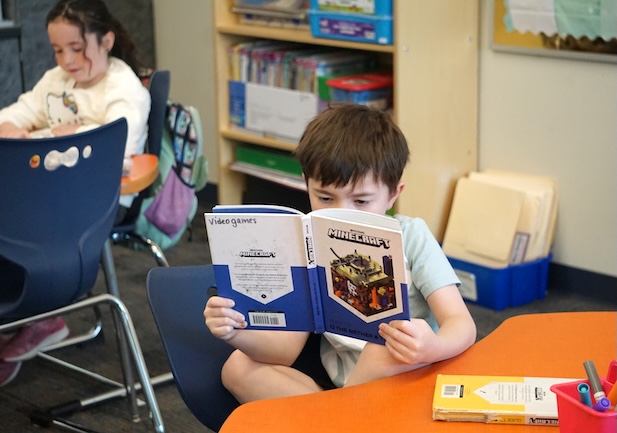 An elementary student reads a book titled "Minecraft"