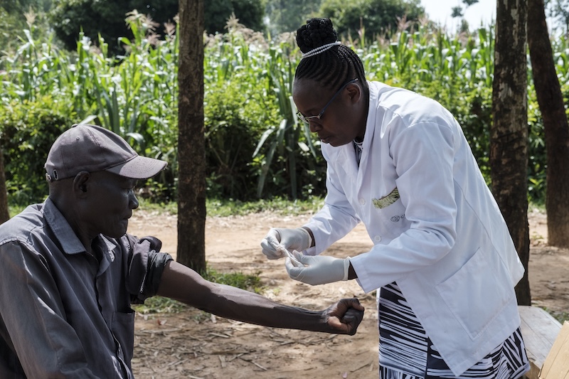 A female doctor, wearing a white lab coat, preps a patient's arm (extended).