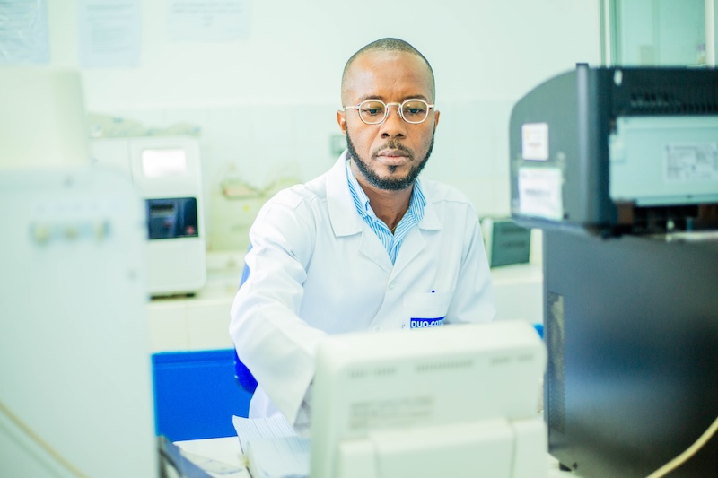 A male doctor, wearing a white lab coat, looks intently at lab equipment.
